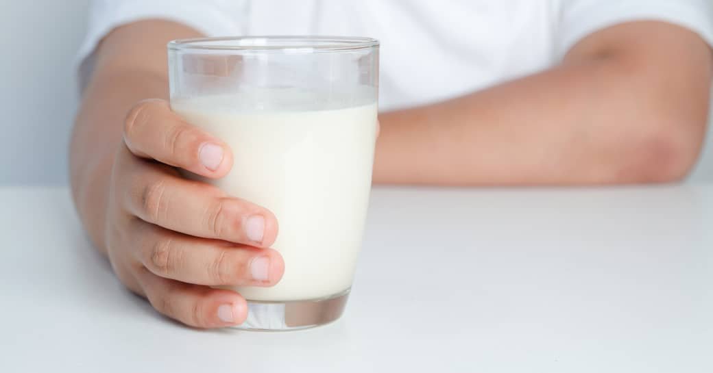una mano humana sujetando un vaso de fresca leche COVAP