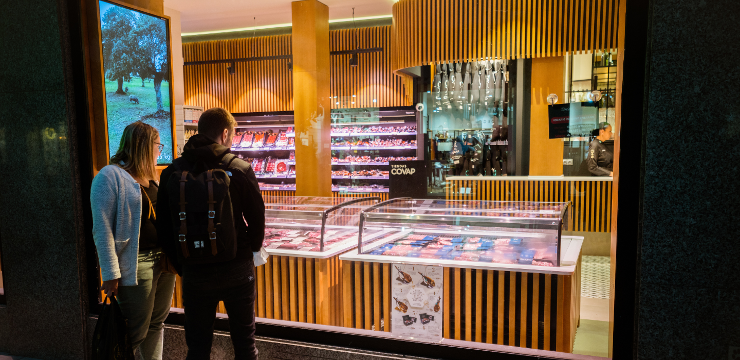 Carnicero de COVAP cortando con delicadeza jamón mientras una clienta le mira con asombro